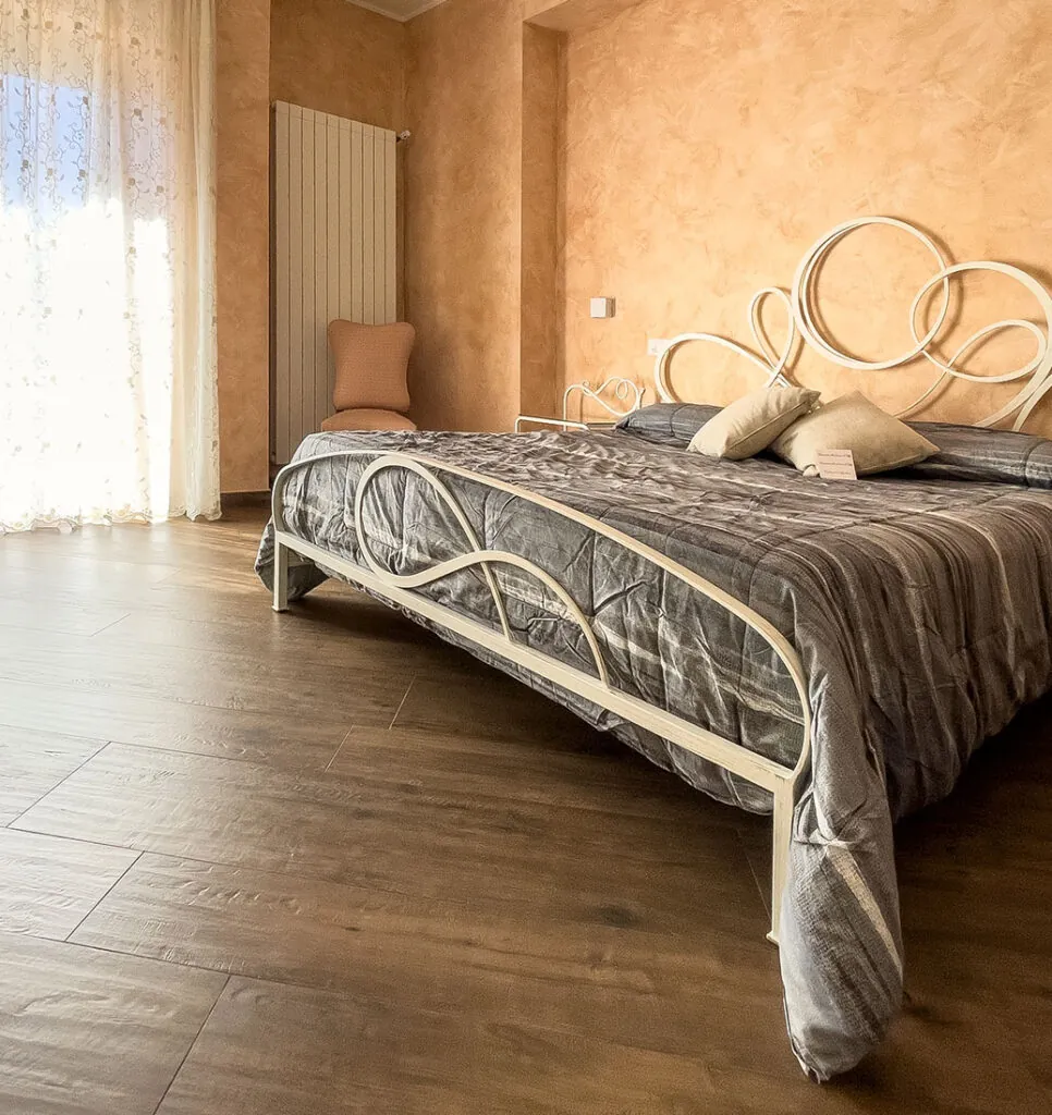 Camera matrimoniale con letto in ferro battuto bianco a volute, copriletto grigio e parete color terracotta