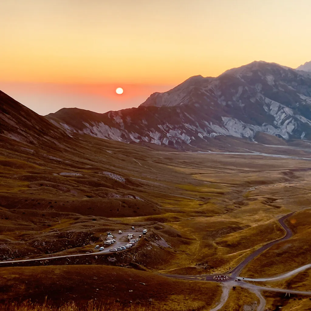 Tramonto su un altopiano di montagna con praterie gialle e una strada che serpeggia in basso
