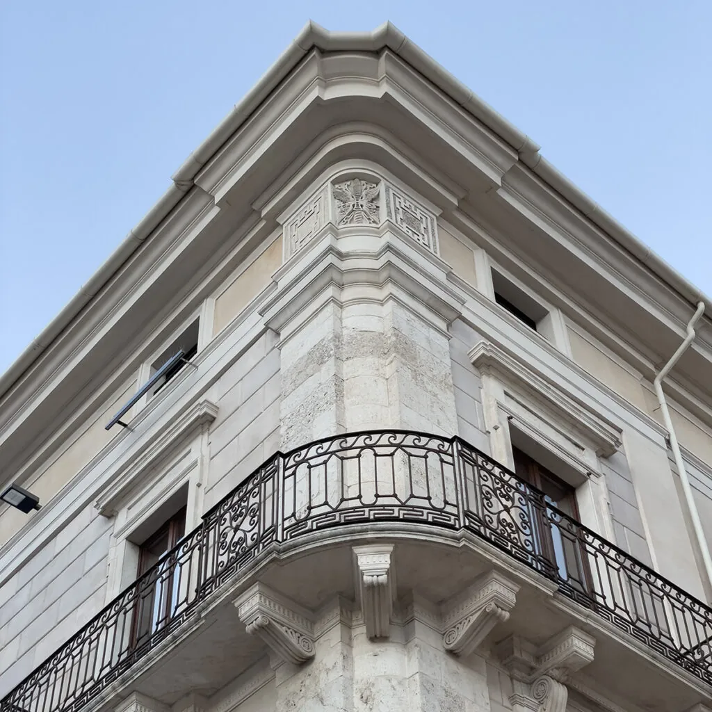 Spigolo di un palazzo storico ripreso dal basso, con cornicione decorato, fregi in pietra e balconi in ferro